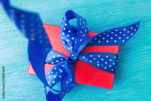 Close up of red gift box with spotted blue bow over wooden background