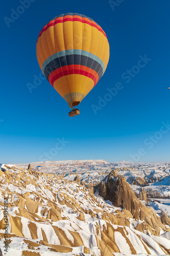 colorful balloon over the extraordinary rocks formations rock hills on snowy winter of Cappadocia, Nevsehir,