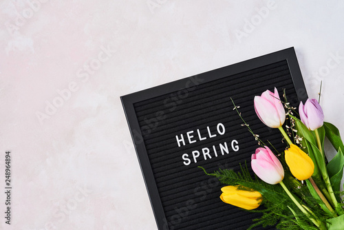 Spring concept. Pink and yellow tulips on letterboard with quote Hello Spring over pink background. Top view with copy space for text. Flat lay. photo