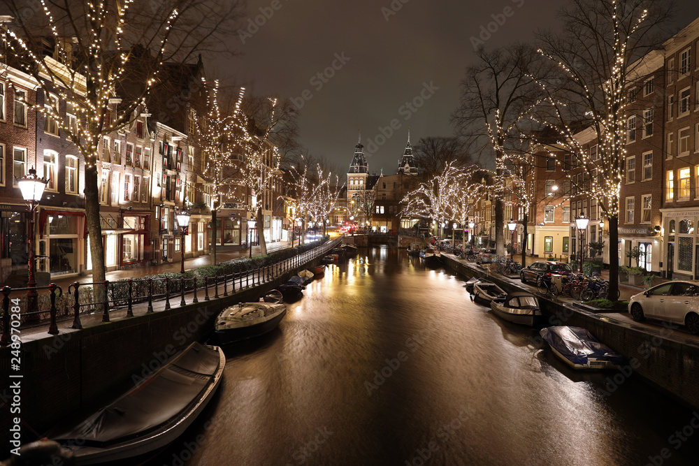 AMSTERDAM, NETHERLANDS - JANUARY 7, 2019: illuminated trees and buildings reflected in water at Spiegelgracht Amsterdam in december by night