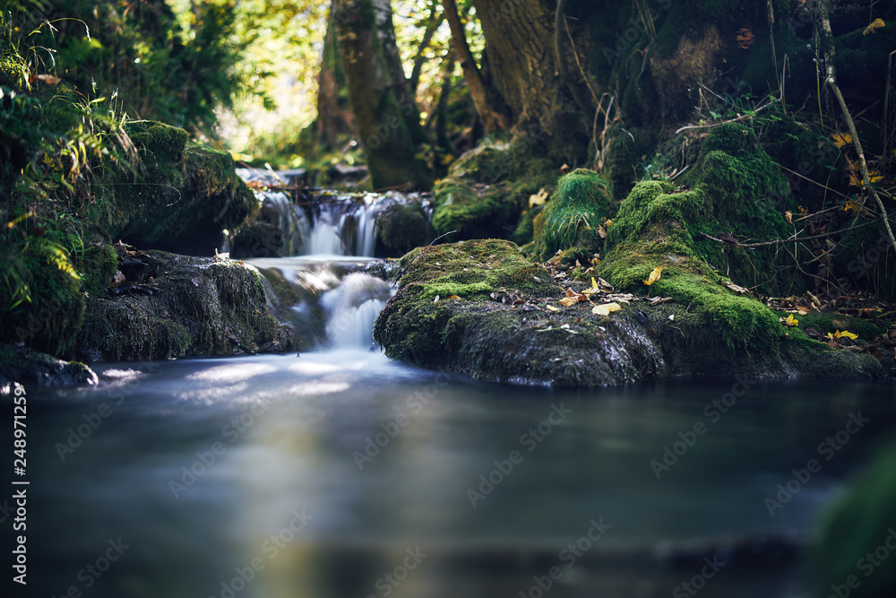 Long exposure of a river creek with a small waterfall. Sunset and strong detail bokeh view. blue calm warm water