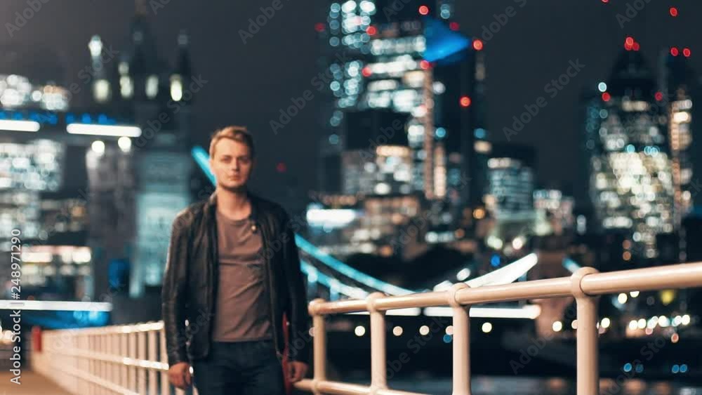 Slow motion young man walking alongside Thames River Tower Bridge London skyline at night Slow motion young man walking alongside Thames River Tower Bridge London skyline at night