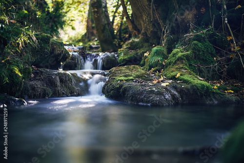 Long exposure of a river creek with a small waterfall. Sunset and strong detail bokeh view. blue calm warm water