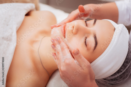 Pleasant young woman having a foam face massage photo