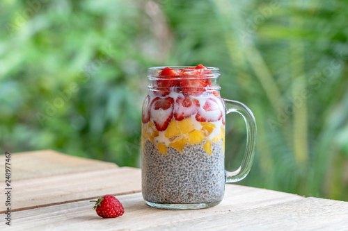 Almond milk chia pudding with fresh strawberries and mango in a glass jar mug. Vegan raw breakfast. Chia seeds and fresh cut fruits and berries dessert
