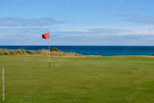 Golf flag on green with sea in background at Port Fairy golf course in Victoria Australia