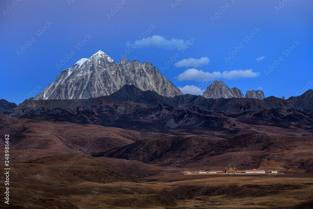 Tagong Prairie Grassland, Lhagang Grassland, Tibetan area of Sichuan Province China. Buddhist Monastery in foreground, Yala Snow Mountain towering in the distance. Twilight, martian alien landscape