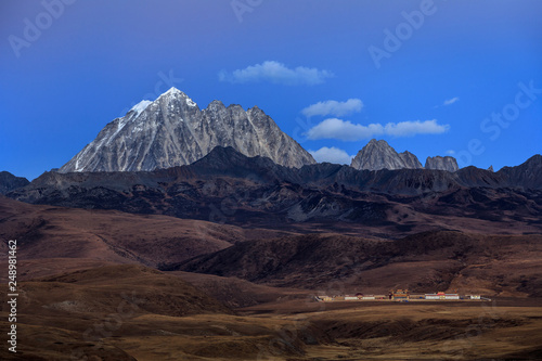 Tagong Prairie Grassland, Lhagang Grassland, Tibetan area of Sichuan Province China. Buddhist Monastery in foreground, Yala Snow Mountain towering in the distance. Twilight, martian alien landscape