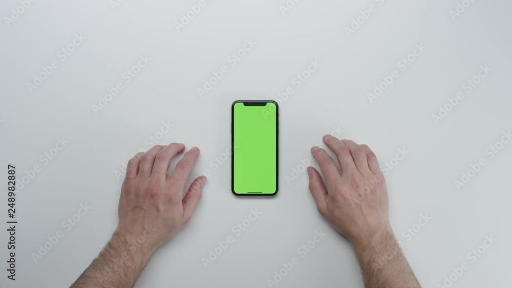 Male hands using smart device with green screen chroma on white clean minimalistic table with top view