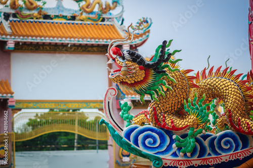 Beautiful large grimace dragons crawling on the decorative tile roof in Chinese temples. Colorful roof detail of traditional Chinese temple with dragon statue on blue sky background.