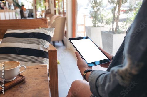 Mockup image of woman holding black tablet pc with blank screen with coffee cup on wooden table in cafe