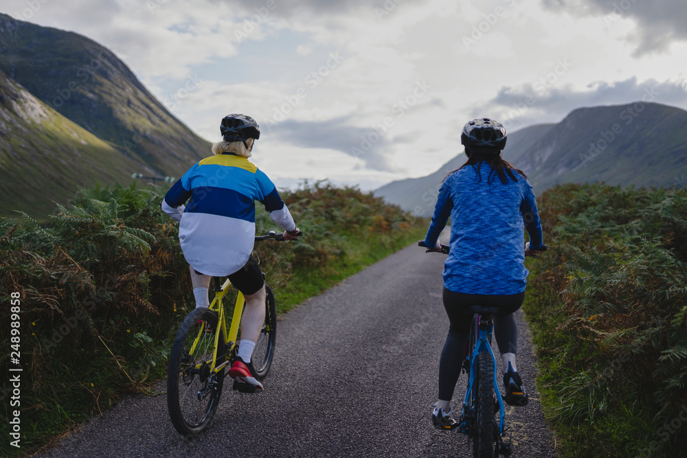 Fototapeta premium Couple cycling down a road in the Scottish Highlands