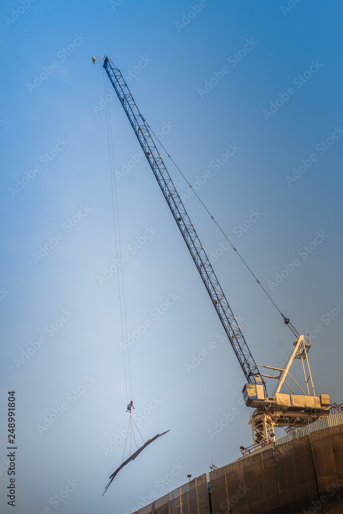 View of construction of multi-storey residential building. Condominium under construction with the luffing jib crane. High-rise skyscraper building construction site with crane against bright blue sky