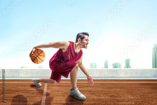 Young asian man basketball player posing in dribbling the ball between the legs on outdoor basketball court
