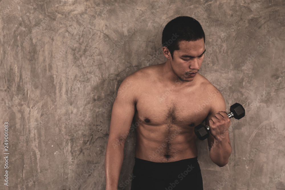 Portrait of Attractive young man with dumbbell on grunge background.