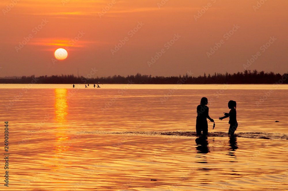 Happy children playing on the beach at sunset