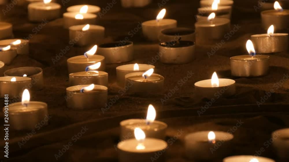 A large number of small white round candles burning in the sand. Background of burning wax candles A large number of small white round candles burning in the sand. Background of burning wax candles