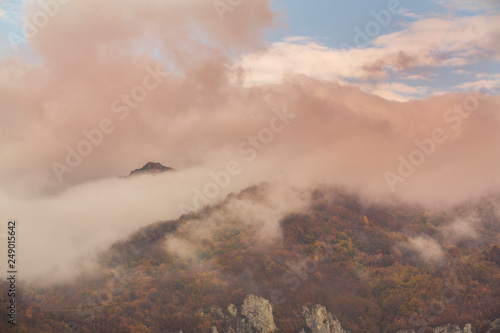 Beautiful autumn scenery in the mountains with mist clouds, pine trees and colorful foliage © Calin Tatu