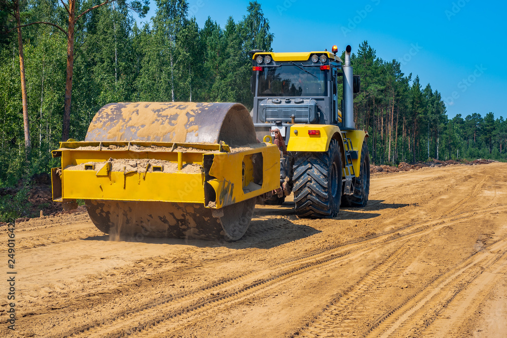 Pneumatic-tired roller compacts the soil in the embankment on the road's construction. sand consolidation on road-building. Yellow compactor driving on the sandy roadbase. soil compacting machine Pneumatic-tired roller compacts the soil in the embankment on the road's construction. sand consolidation on road-building. Yellow compactor driving on the sandy roadbase. soil compacting machine