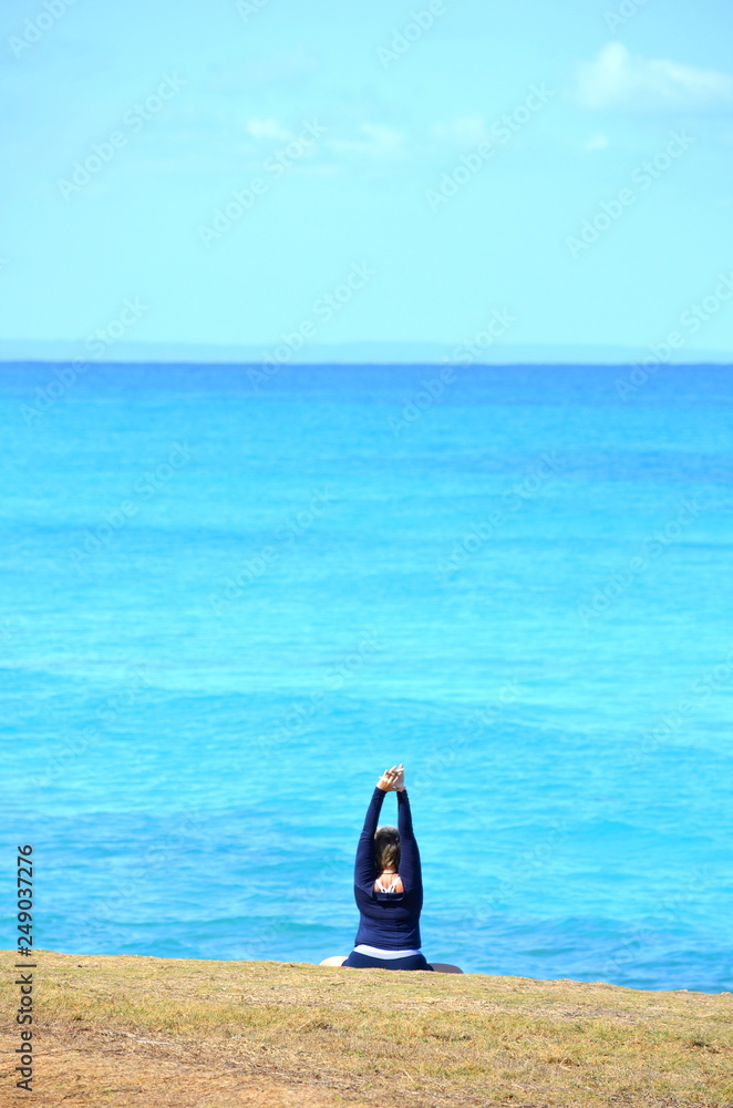 Plus size woman with short hair meditating and practicing yoga on a tropical beach. Solo traveller enjoying vacation.  Leisure, recreation, travel, self-care and lifestyle theme.