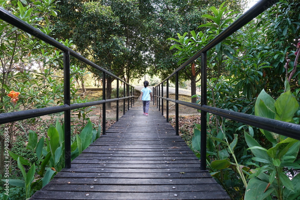 Obraz premium Unidentified child is walking through a wooden bridge in the park.