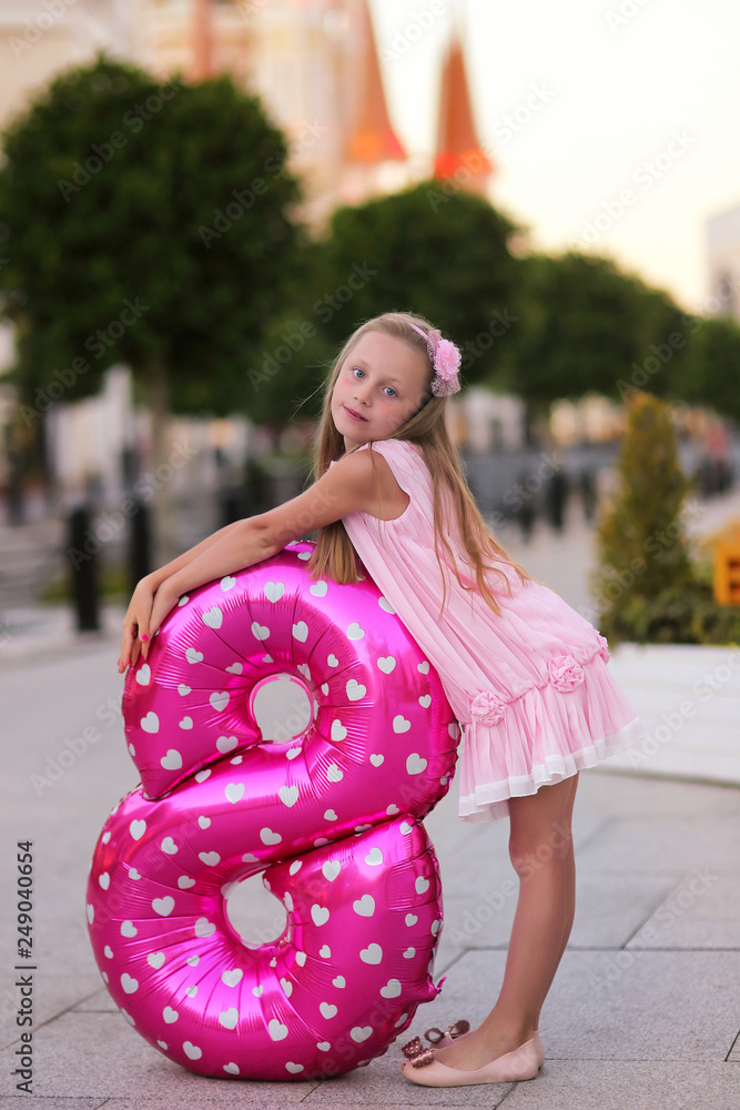 Children's birthday. Smiling a beautiful blond little girl with a helium ball in the form of a figure eight celebrates her birthday