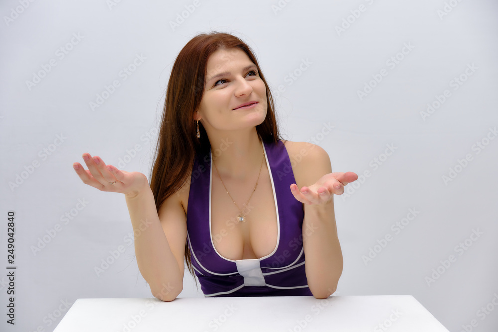Concept studio Portrait of a beautiful young brunette girl sitting at the table on a white background and talking in different poses. Concept studio Portrait of a beautiful young brunette girl sitting at the table on a white background and talking in different poses.