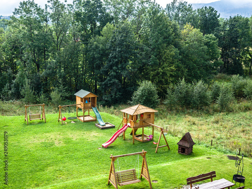 Outdoor playground for children with forest trees, grass and mountains.
