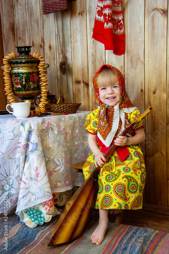 a little girl in russian folk clothes at the celebration of the slavic holiday of maslenitsa sitting at the table and holding a balalaika