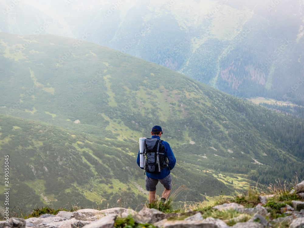 A man back with backpack for camping is trekking on a mountain having fun, walking along the distance on his holiday at Tatra mountain, Poland, Slovakia.