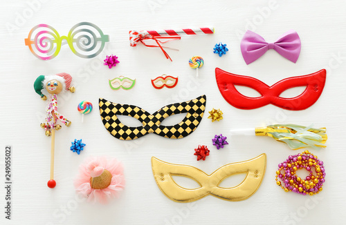 carnival party celebration concept with mask and colorful party accessories over white wooden background. Top view.
