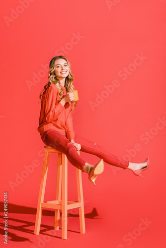 happy stylish girl with cup of coffee sitting on stool on living coral. color of the year 2019 concept