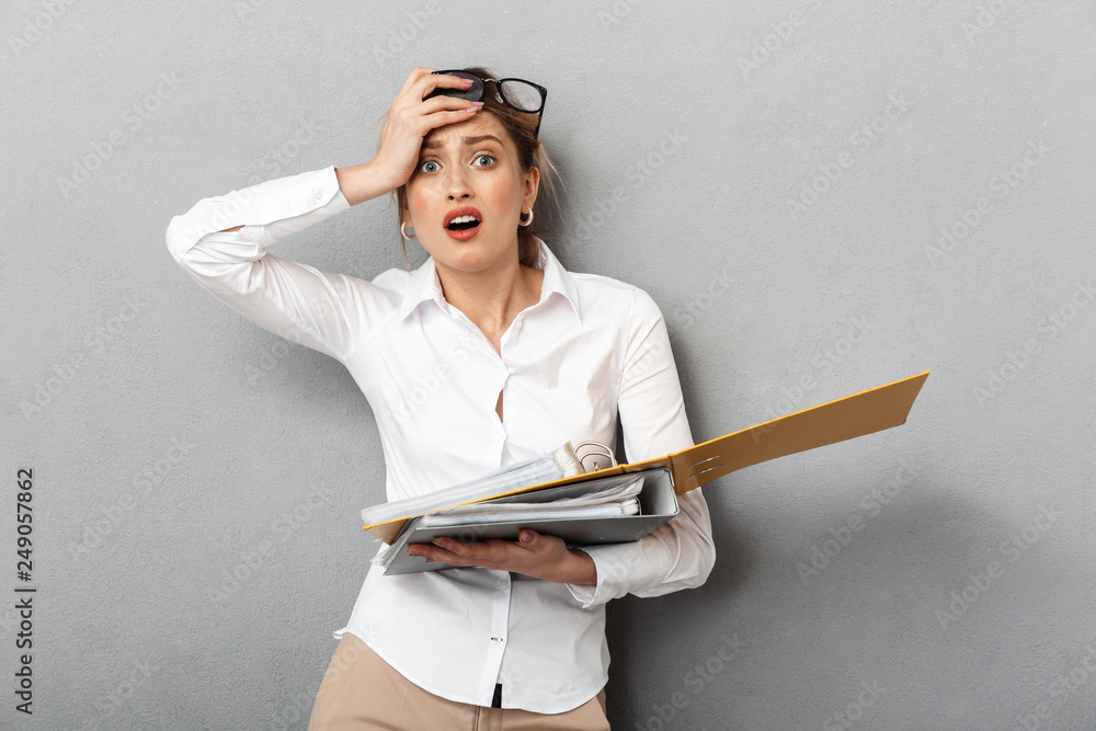 Confused business woman isolated over grey wall background holding folders. Confused business woman isolated over grey wall background holding folders.