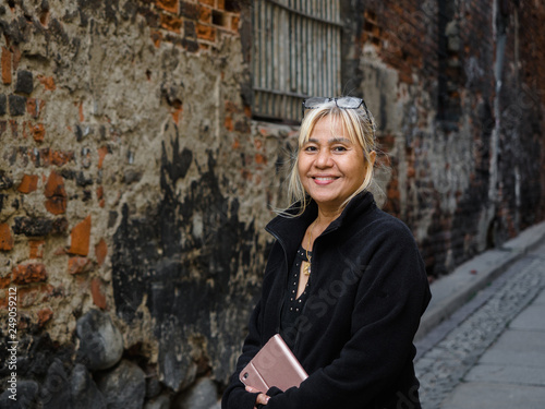 60 years old age Asian Thai woman with technology smart tablet, mobile phone, and glasses on her head traveling in Europe old beautiful city view on background for holiday.