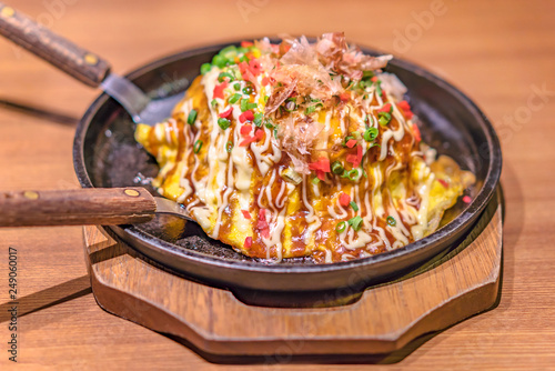 Japanese okonomiyaki covered with katsuobushi leek mayonnaise and bulldog sauce served on a hot plate with spatulas.