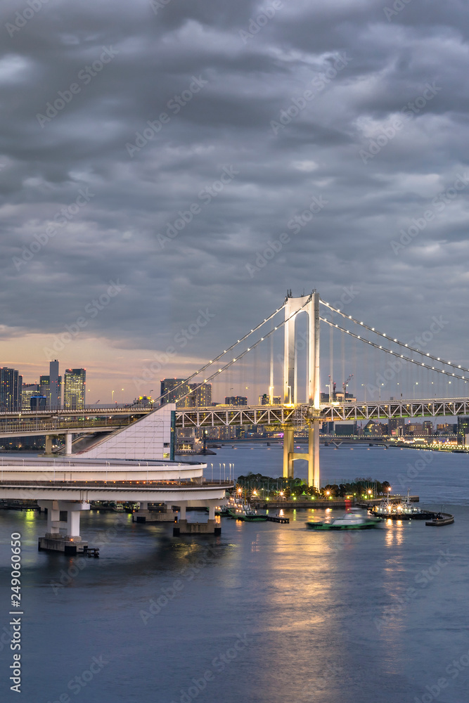Circular highway leading to the Rainbow Bridge with Cargo and cruise ships moored or sailing in Odaiba Bay of Tokyo.
