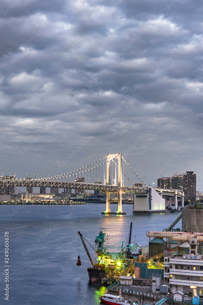 Rainbow Bridge with Cargo and cruise ships moored or sailing in Odaiba Bay of Tokyo.