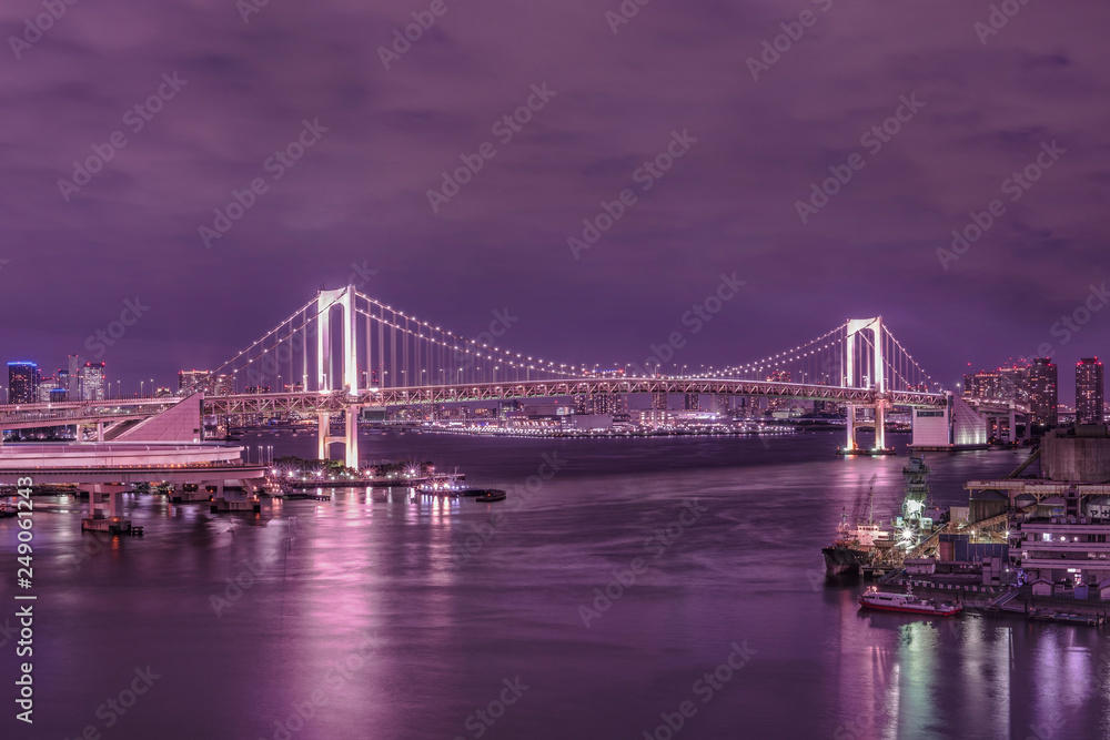 Fototapeta premium Circular highway leading to the Rainbow Bridge with Cargo and cruise ships moored or sailing in Odaiba Bay of Tokyo.