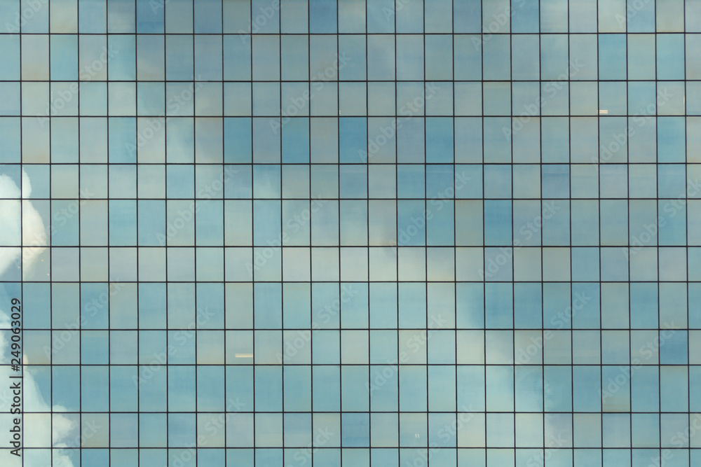 Glass wall texture. This is a detail of the facade of a modern building covered entirely by glass panels that creates a pattern of lines and sky reflection Glass wall texture. This is a detail of the facade of a modern building covered entirely by glass panels that creates a pattern of lines and sky reflection