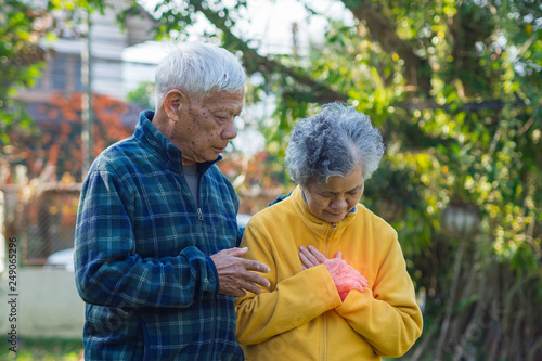Portrait of elderly man with his wife suffering from chest pain a home garden. Healthcare Concept.