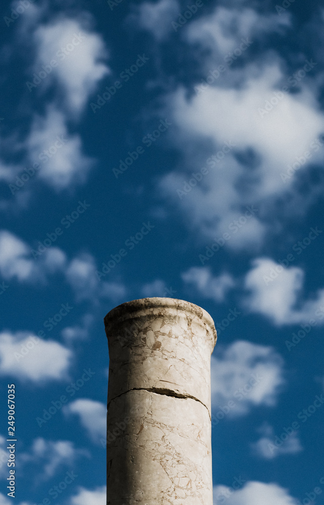 Ancient column on the background of bright blue sky with clouds.