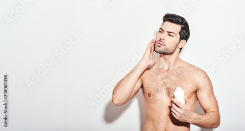 Another beauty treatment. Handsome man applies the moisturizer standing isolated over white background