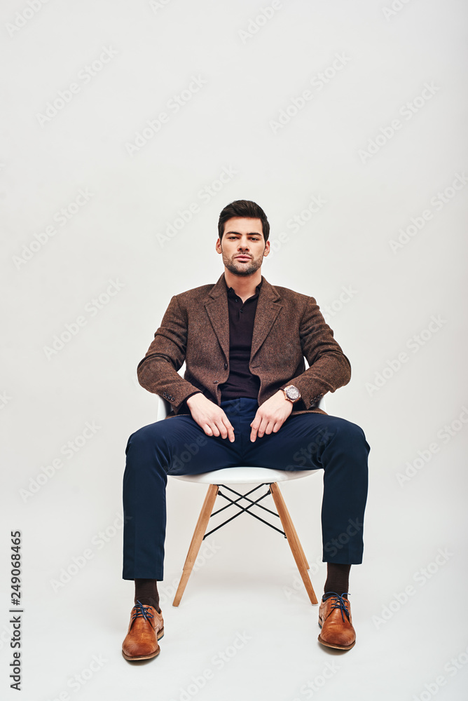 Total control. Stylish dark-haired man sitting on a chair, leaning back and looking at camera isolated over white background Total control. Stylish dark-haired man sitting on a chair, leaning back and looking at camera isolated over white background