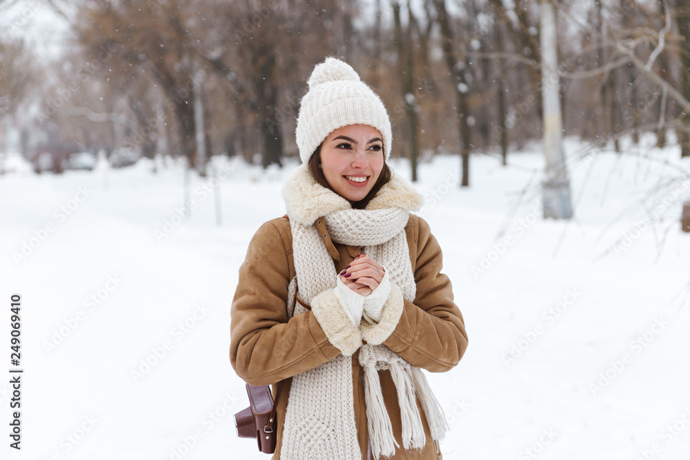 Fototapeta premium Beautiful young woman in hat and scarf walking outdoors in winter snow.
