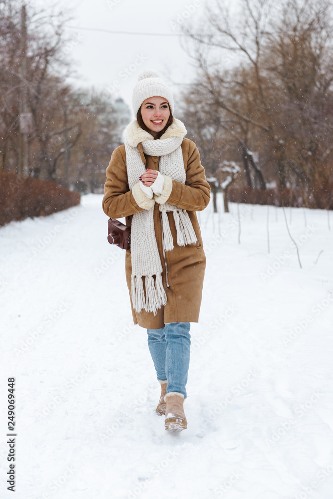Young woman in hat and scarf walking outdoors in winter snow.