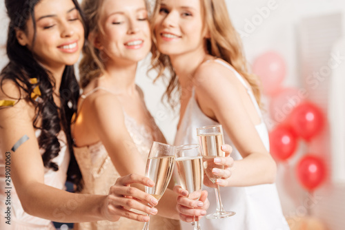 selective focus of champagne glasses with beautiful smiling multicultural girls in nightwear on background