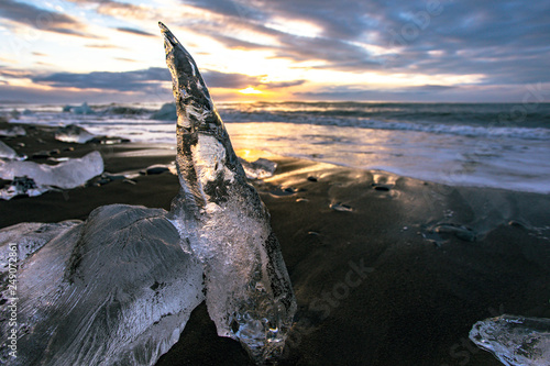 Ice cliff with a black sandy beach on Jokulsarlon beach (Diamond Beach) in southeast Iceland. Ice in the light of the rising sun photo