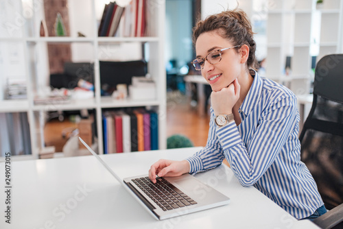 Beautiful young woman with curly hair and eyeglasses using laptop.