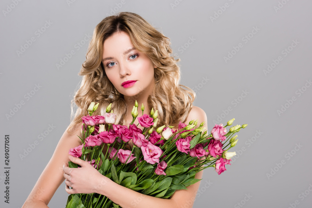 naked beautiful blonde woman posing with spring Eustoma bouquet isolated on grey