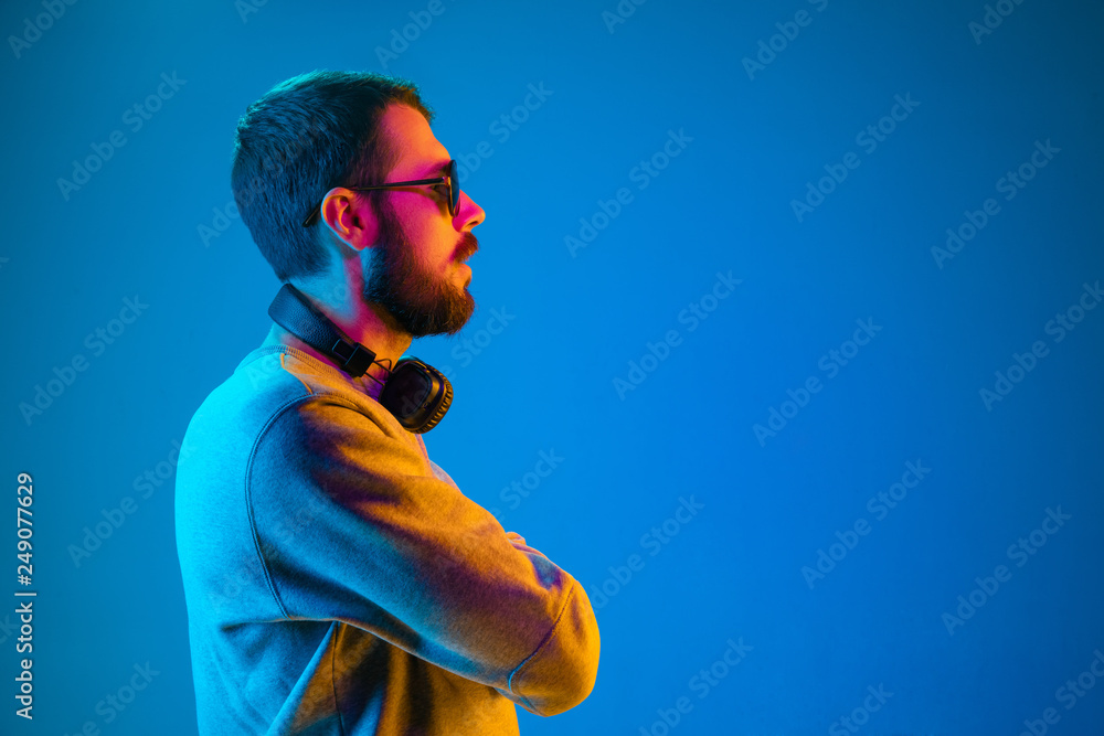 Enjoying his favorite music. Serious young stylish man in sunglasses with  headphones listening sound while standing against blue neon background  Stock Photo | Adobe Stock